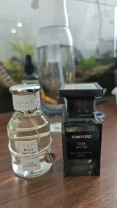 A side-by-side comparison of the luxury fragrance Tom Ford Oud Wood Men bottle (dark glass) and the cost-effective alternative imixx perfume No. 48 in its minimalist bottle